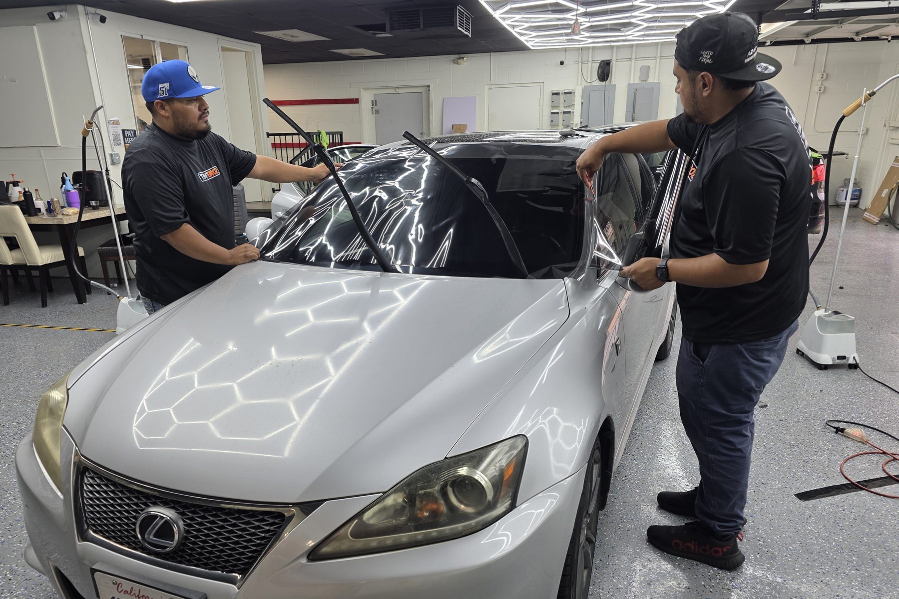 Two Tint Broz installers aligning window film across a vehicle windshield inside the shop